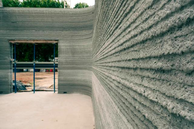 The 3D printer stacks layers of concrete like icing on a cake.